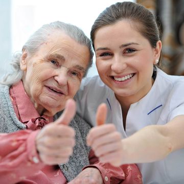 Ein Foto von einer alten Frau und einer Pflegerin mit Daumen hoch.